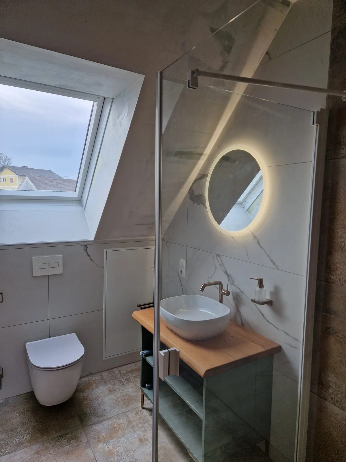 Badezimmer mit wandhängendem WC, rundem beleuchtetem Spiegel und Marmorfliesen